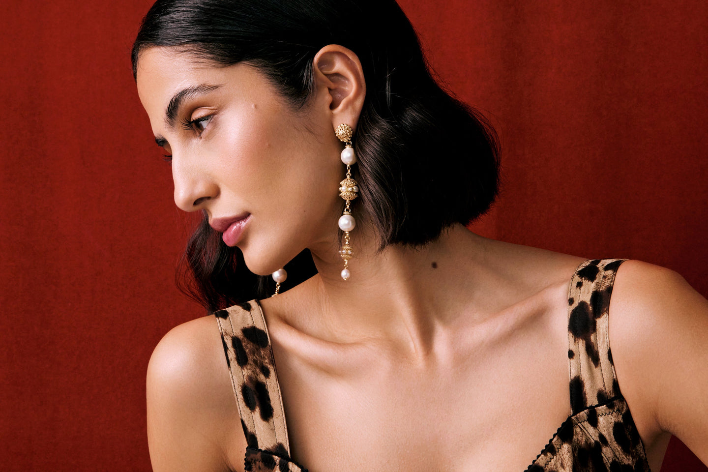 Model wearing big gold heart earrings in lace top, with red background. Promoting the Soru Palermo collection of jewellery 