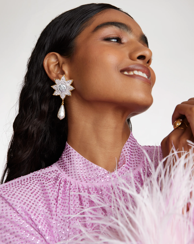 Lady wearing pink sequin dress with feather sleeves and sparkly flower earrings with drop pearl