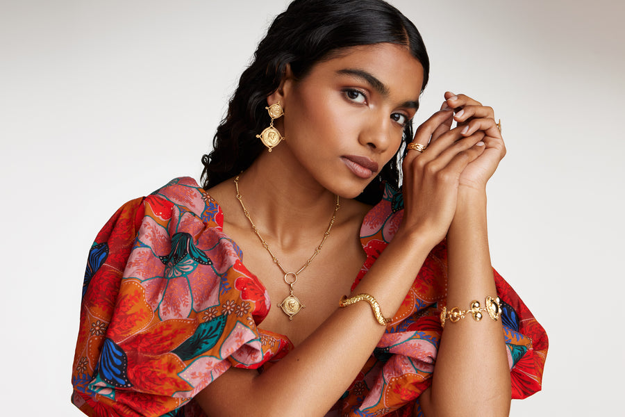 Model image wearing soru jewellery double coin earrings  with matching charm on a chain with two chunky gold bracelets and a gold ring