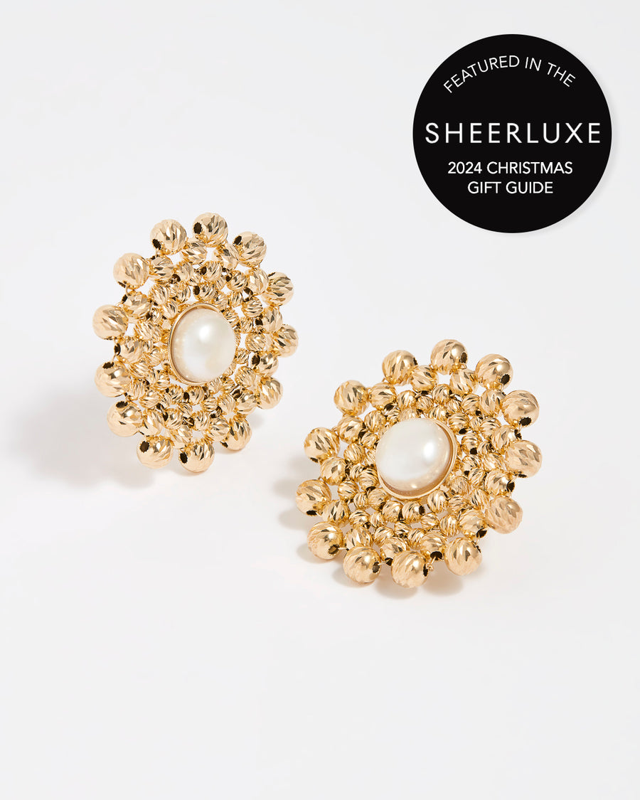 Close up product shot of gold flower shaped beaded earrings featuring a centre pearl gemstone on a white background