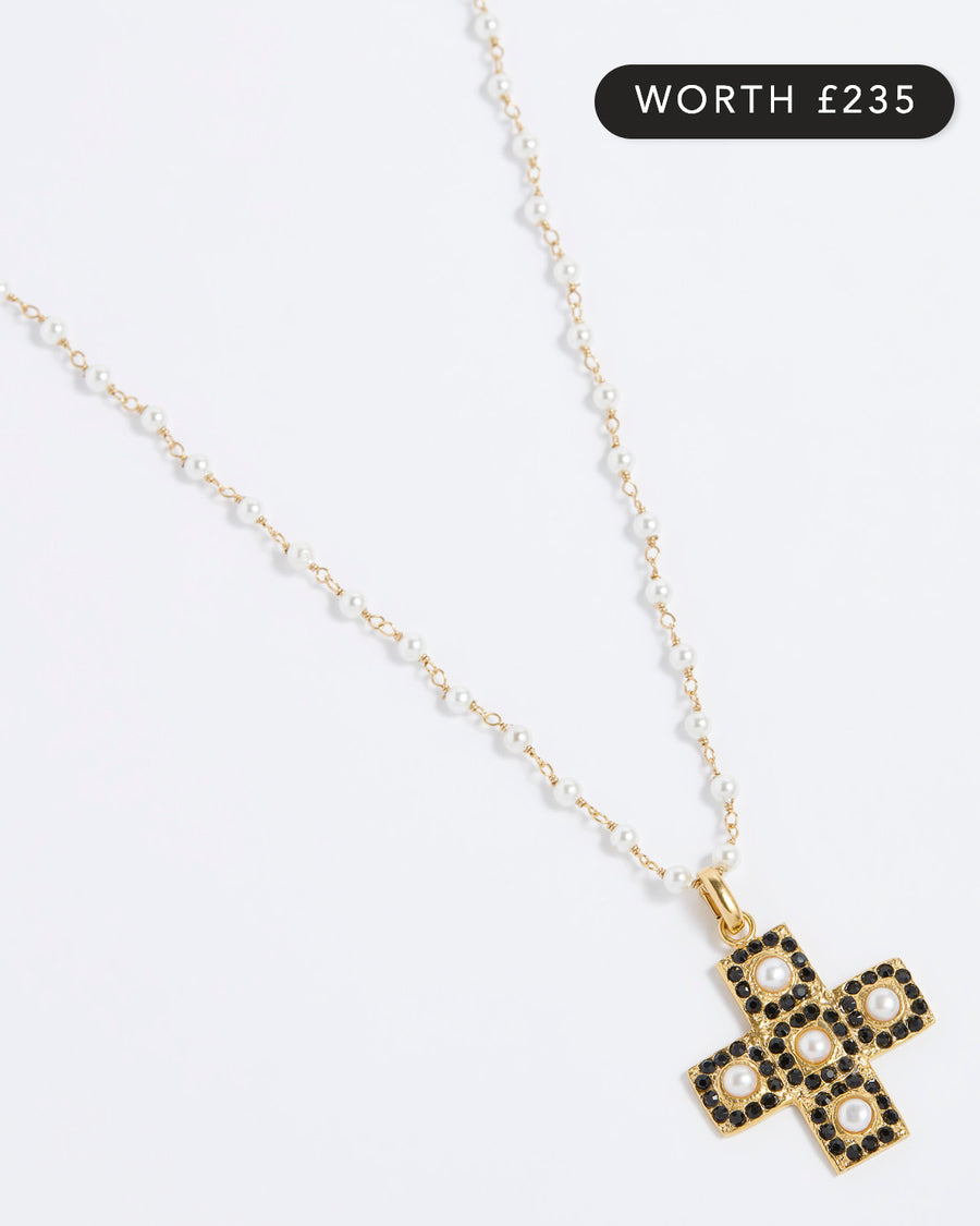 Product image of a gold textured cross-shaped pendant embellished with alternating baroque pearls and black crystals hung from a Soru pearl charm chain on a white background.