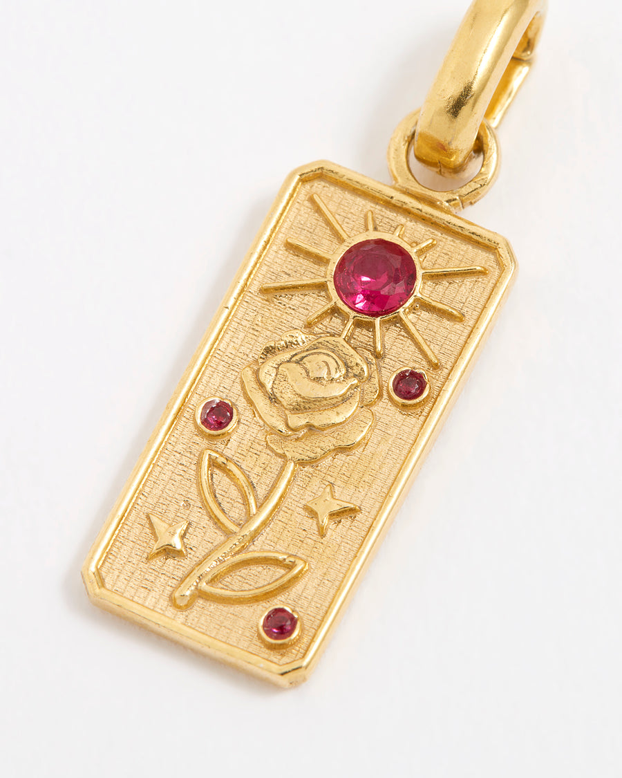 Close up shot of a rectangular gold textured charm with engraving of a rose and scattered red gemstones