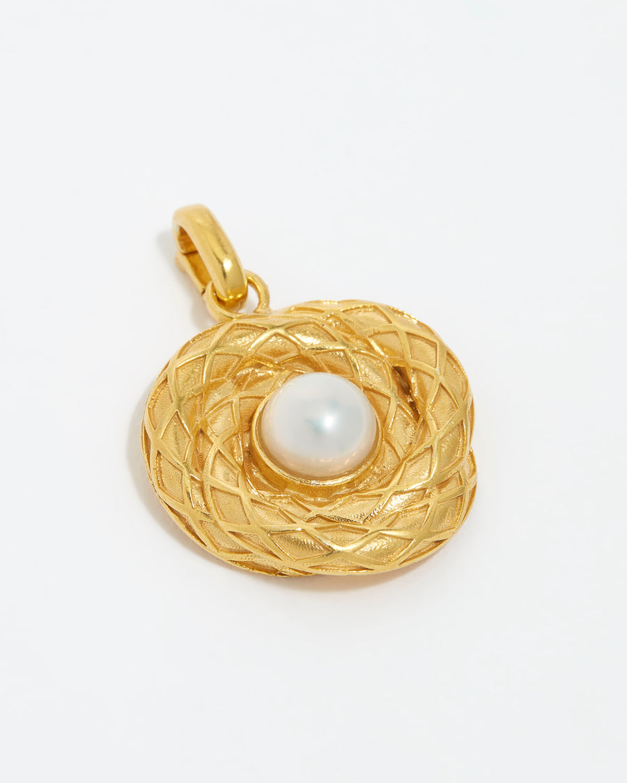 close up image shot of gold textured charm with centre pearl on a white back ground