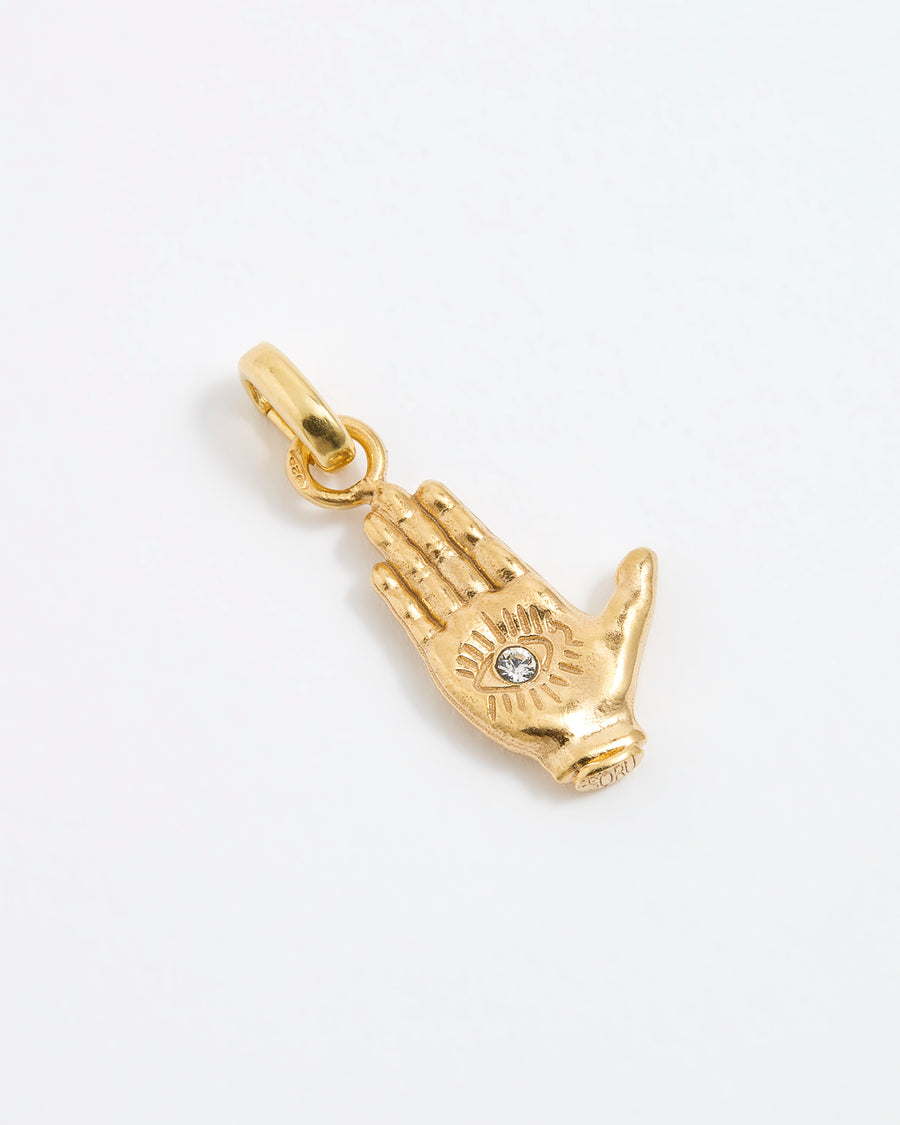 Product shot of a gold hand-shaped charm featuring an inset eye symbol in the palm, set with a clear crystal.