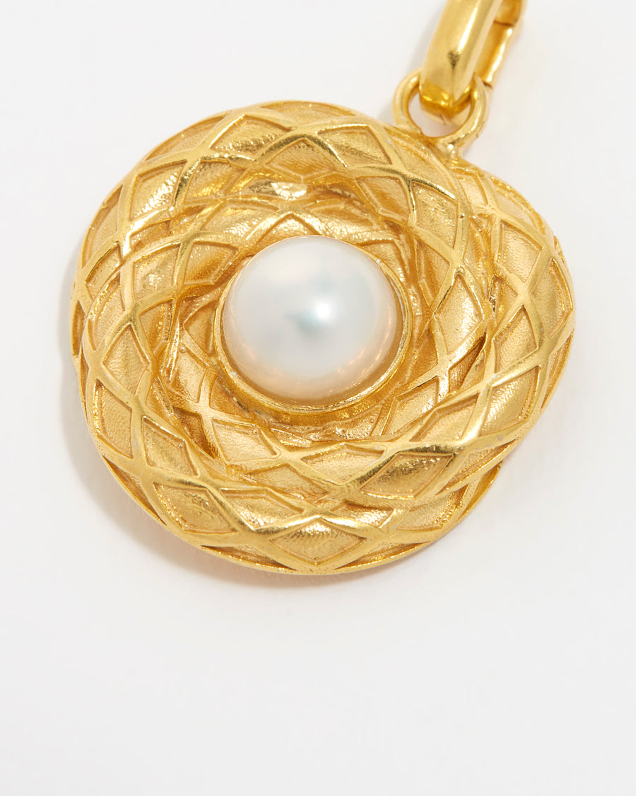 Close up overhead image of the gold textured charm with pearl centre on white background