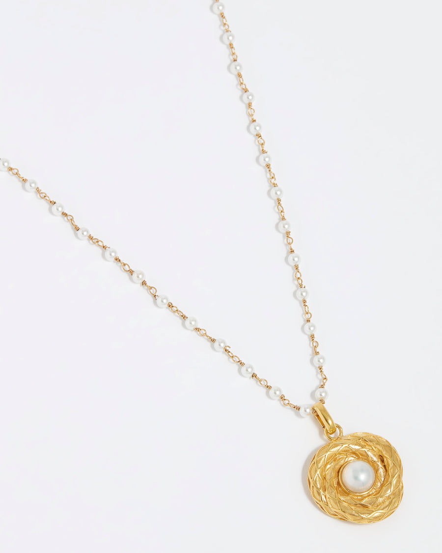 Product shot image of gold textured charm with pearl centre hung from a pearl chain on white background