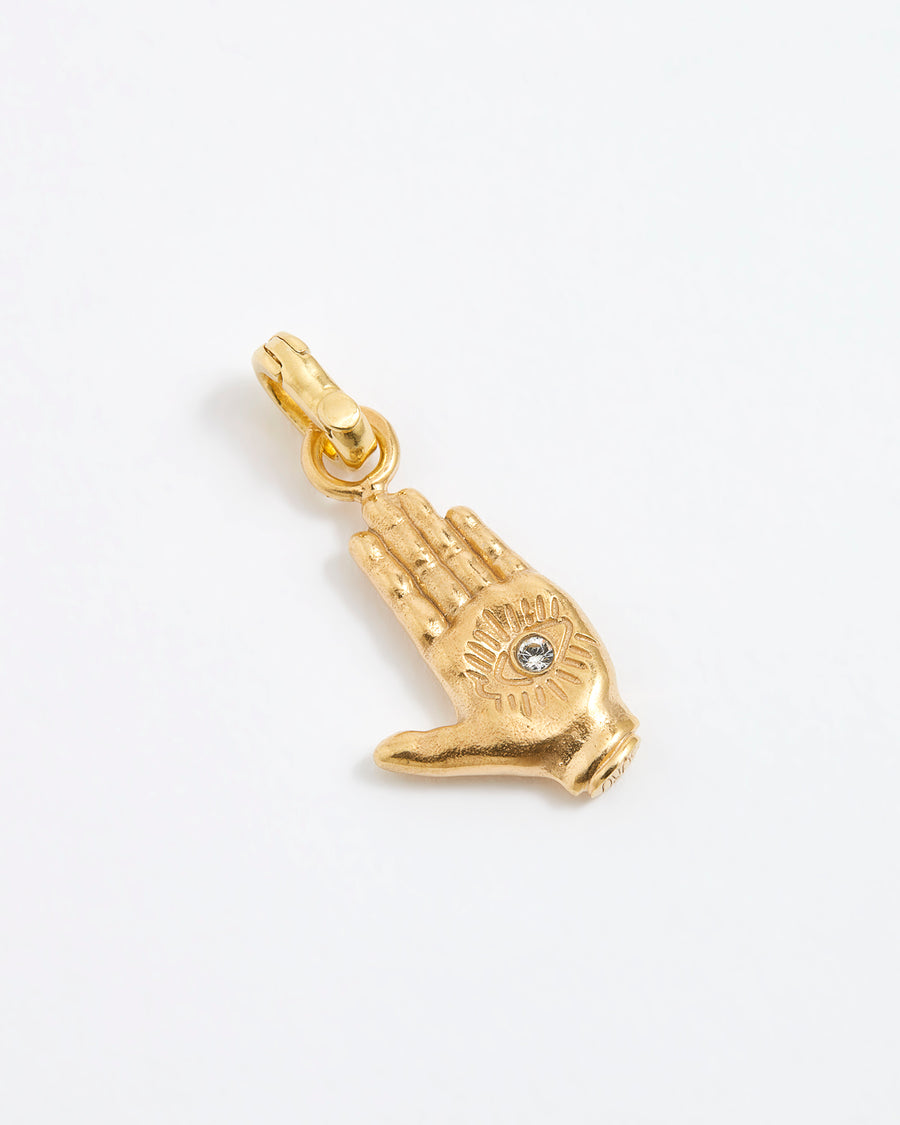 Close up shot of a gold hand-shaped charm featuring an inset eye symbol in the palm, set with a clear crystal.