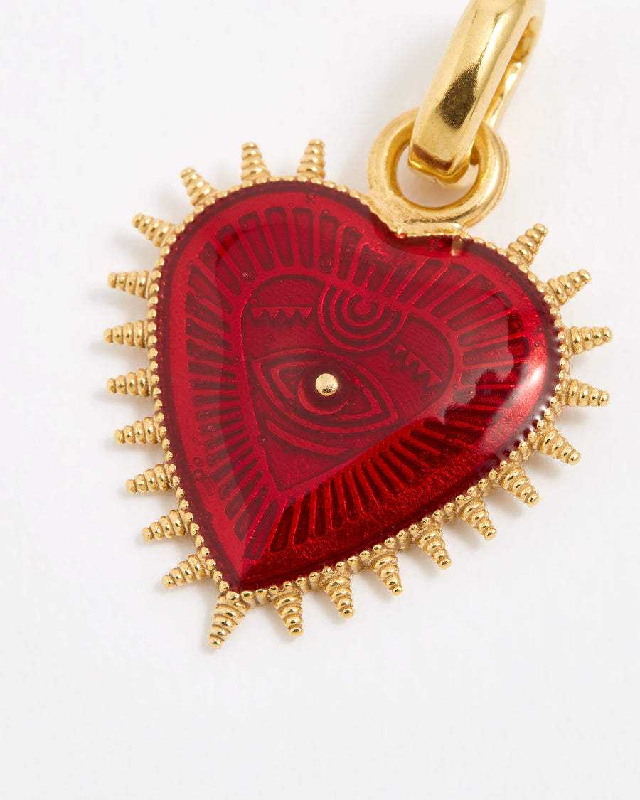 Close up product shot of a heart-shaped pendant featuring a deep, glossy red patterned enamel centre. The heart is surrounded by a border of gold spikes that extend outward from the edges.