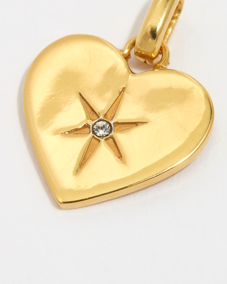 close up image shot of a clear crystal surrounded by a star etching set in a shiny gold heart on a white background