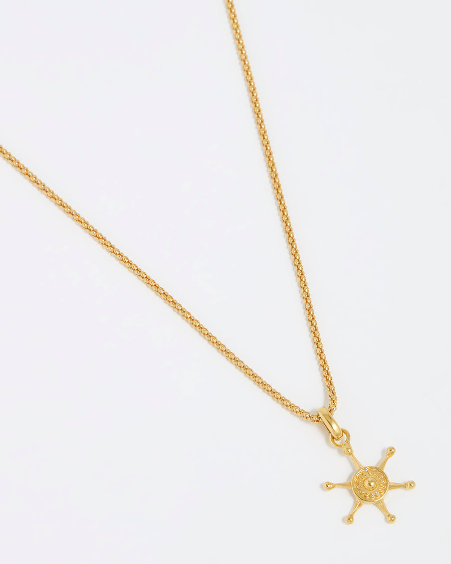 Product shot of gold ships wheel charm hung from a rope chain on a white background