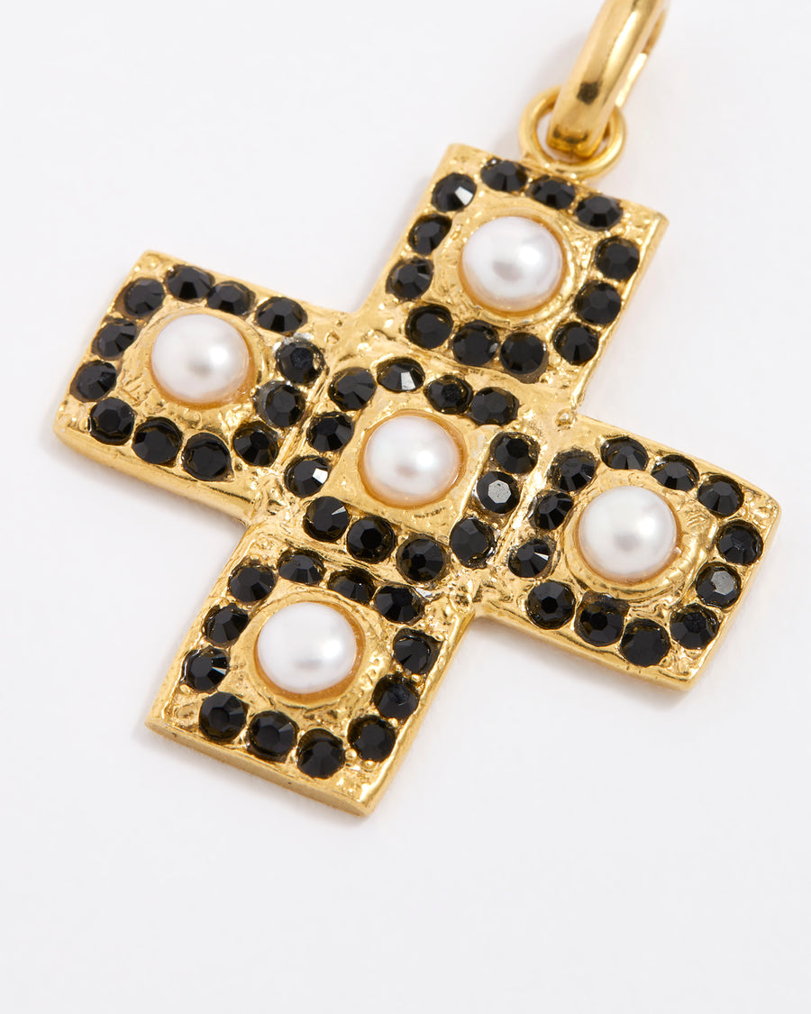 Close up overhead image of the gold textured cross-shaped pendant embellished with alternating baroque pearls and black crystals on a white background.