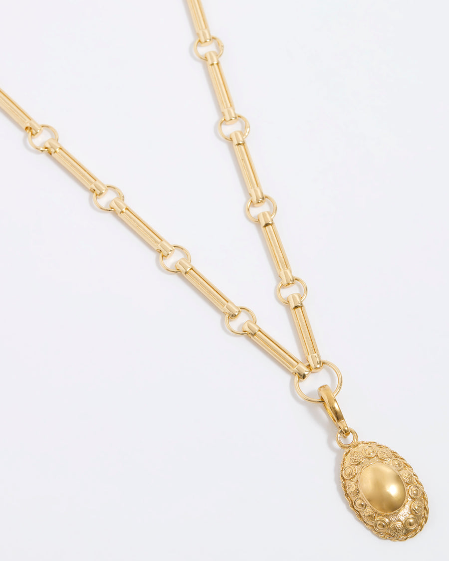 Gold oval charm with intricate embossed patterns and a smooth central dome, paired with a gold link chain necklace.