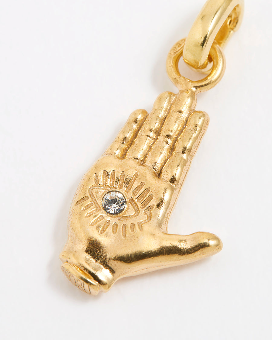 Close up shot of a gold hand-shaped charm featuring an inset eye symbol in the palm, set with a clear crystal.