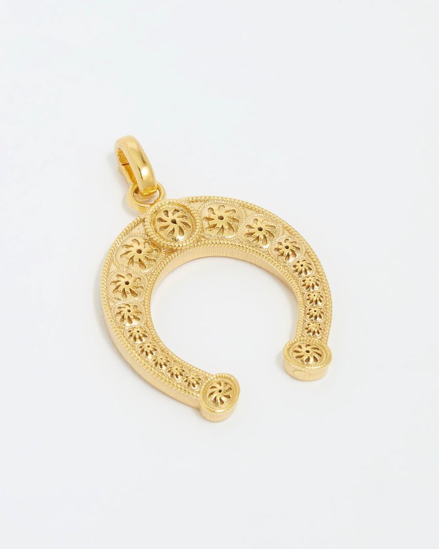 Over top view on white background of gold plated horsehoe charm from Soru Jewellery, Daphne Oz
