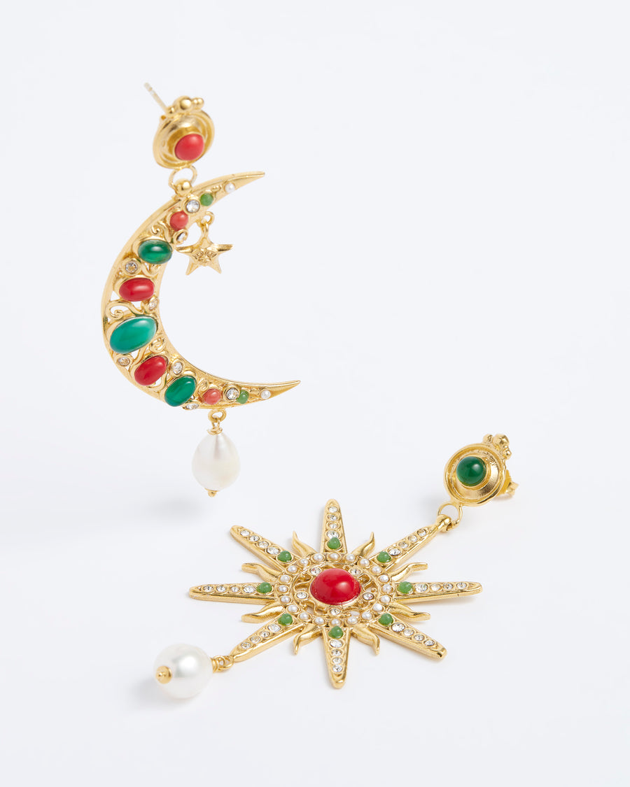 Product shot of mis-matched statement earrings, one featuring a star and the other a crescent moon. Detailed with hanging pearls and colourful green and red stones, on a white background.