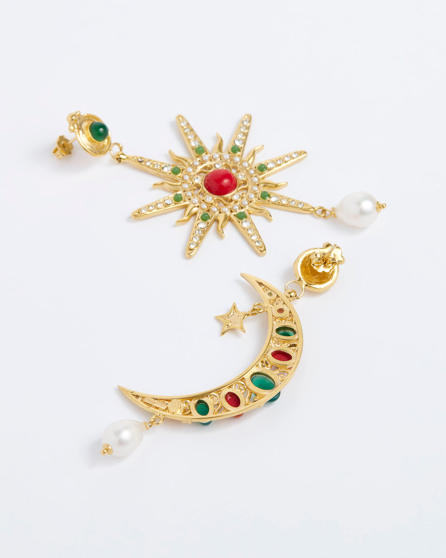 Product shot of mis-matched statement earrings, one featuring a star and the other a crescent moon. Detailed with hanging pearls and colourful green and red stones, on a white background.