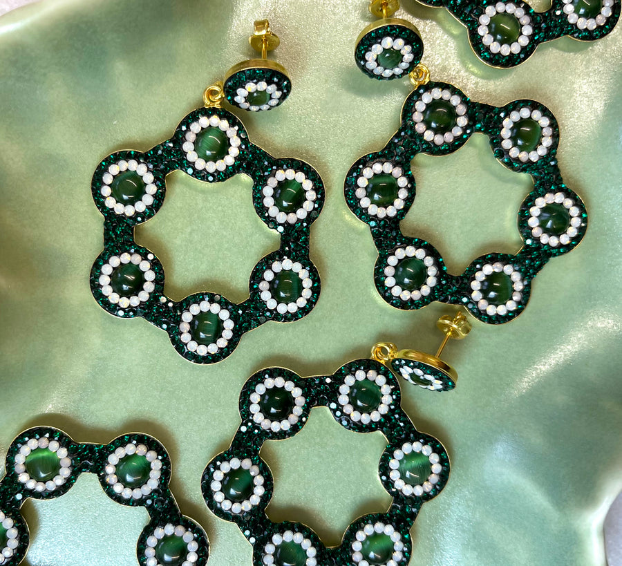 Emerald green hoop earrings with vibrant green cat’s eye gemstones, surrounded by sparkling emerald crystals and white accents, set in 18k gold-plated silver, displayed in a green wave tray