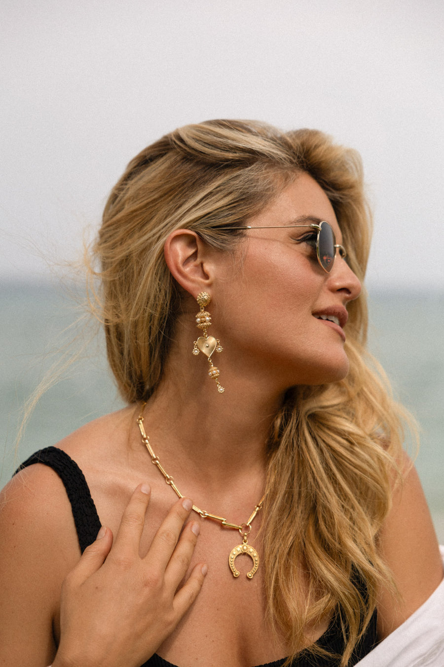 Daphne Oz wearing gold horseshoe charm and necklace outsdie at the beach looking to the side 