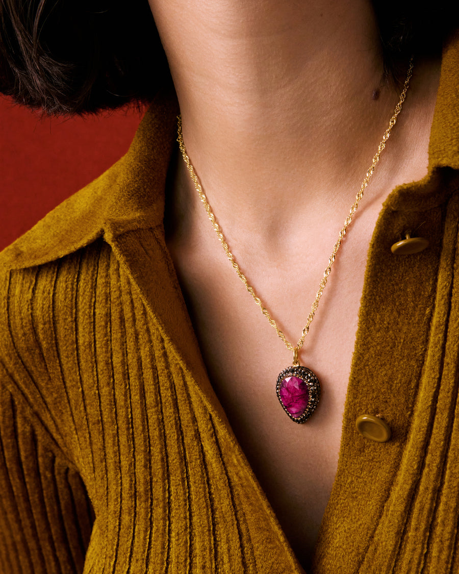 Ruby pear shaped pendant necklace on gold chain with crystal boarder shown close up on models neck 