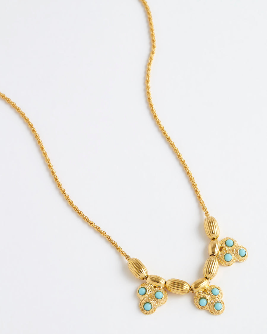 Close up overhead image of the gold rope chain necklace featuring textured gold beads and three turquoise embellished charms on a white background