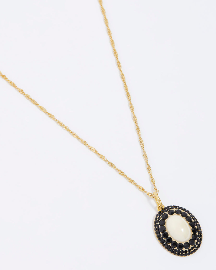 close upside tilted front facing shot on white background of the majorca pearl and black crystal pendant on gold chain 