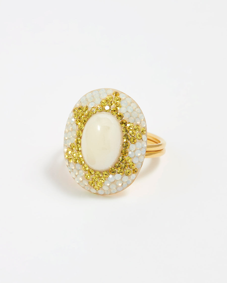 Image of an oval shaped ring featuring an iridescent majorca pearl gemstone surrounded by sparkling golden yellow and opal crystals set as a mosaic sun motif.