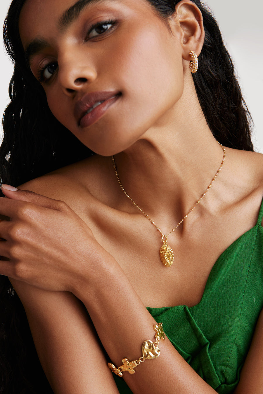 Model shot wearing Soru bracelet features interlocking mixed heart and cross links with a toggle clasp fastening for ease looking forward. Model also wearing seahorse pendant necklace and crystal and gold hoop earrings