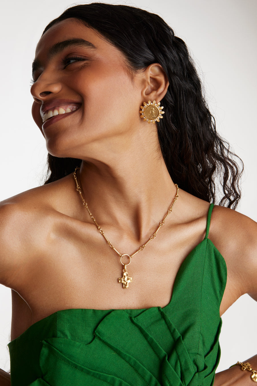smiling model shot wearing soru jewellery detachable gold cross charm on a charm chain whilst wearing coin earrings
