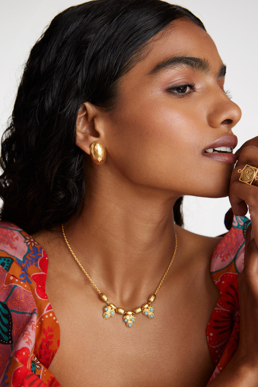 Side view of model shot wearing the gold rope chain necklace featuring gold textured beads and three turquoise embellished beaded charms. Model also wearing gold earrings and ring 