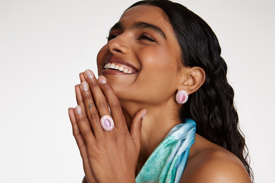 Smiling model wearing Soru Jewellery large pink stud earrings surrounded by crystals and a matching ring