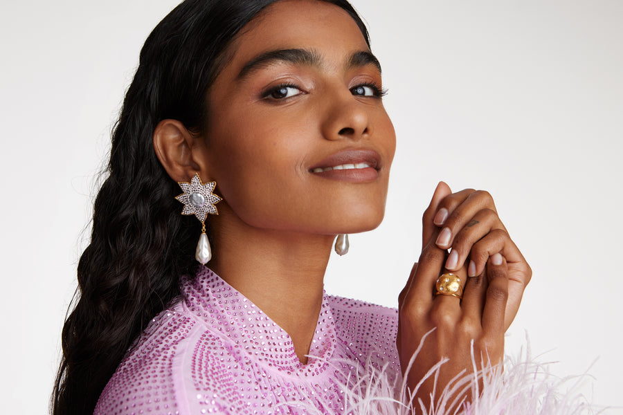 close up model shot of round gold star etched ring with clear crystal embellishment. Model also wearing the large crystal embellished baroque pearl earrings while model smiling