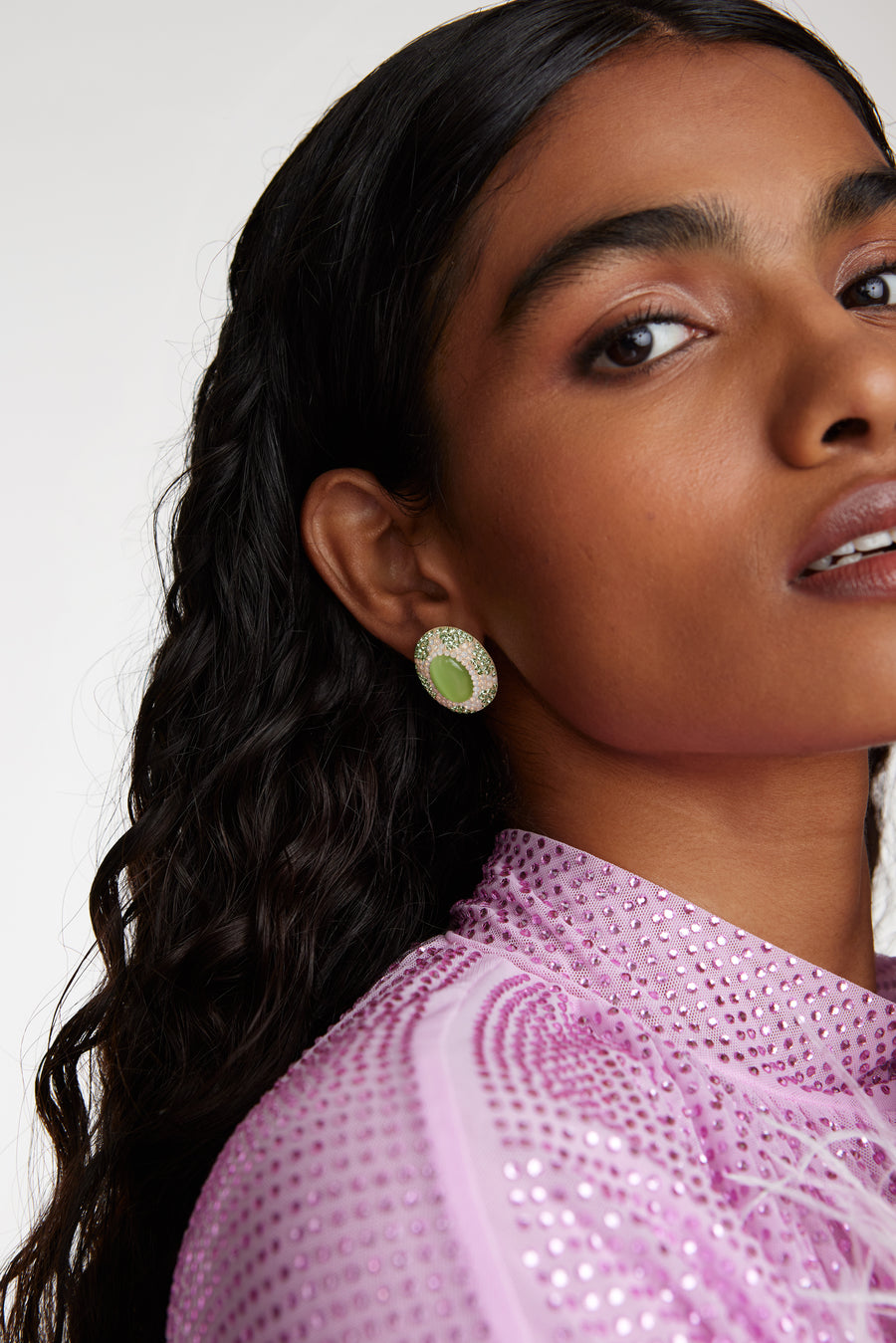 Side view close up model shot wearing oval stud earrings featuring a vibrant green cats eye stone surrounded by sparkling green and opal crystals set with a sun motif 
