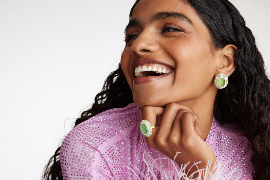 Close up model shot wearing chunky green stone and crystal ring with matching earrings while laughing with hand under chin
