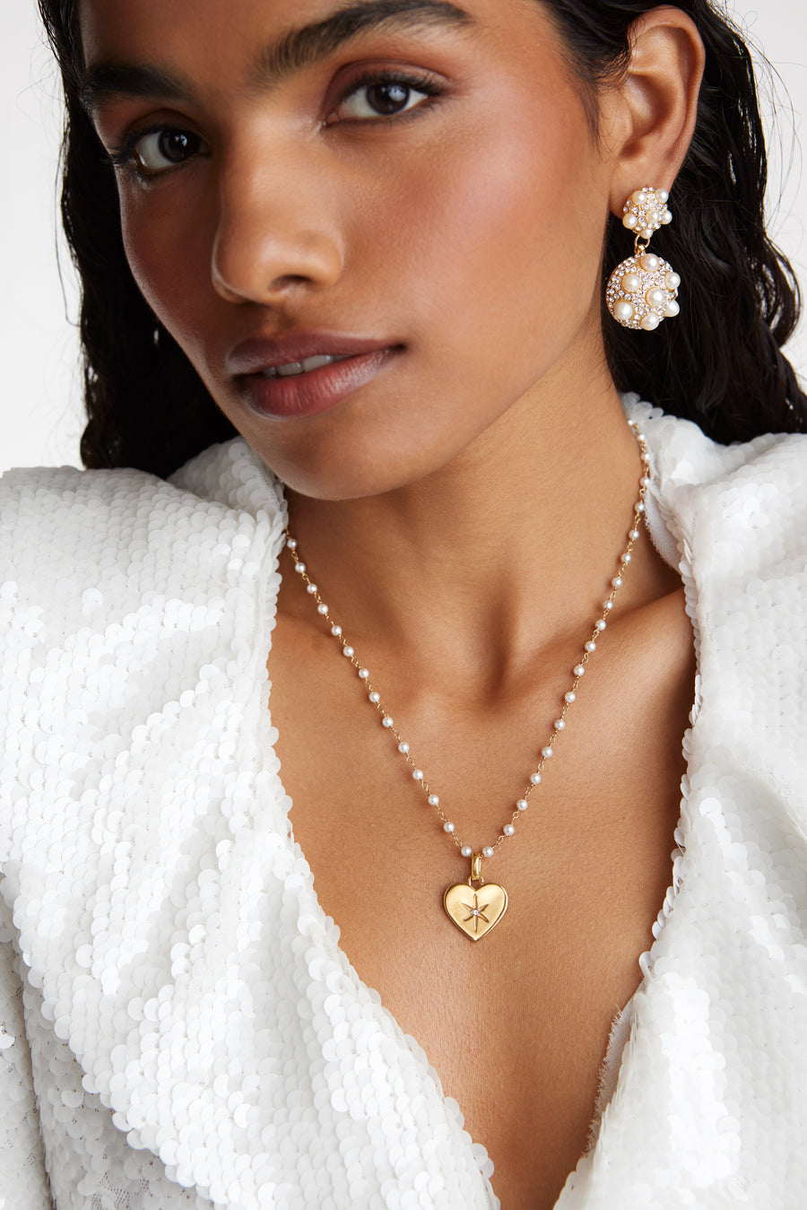 Model shot wearing the Soru Jewellery clear crystal surrounded by a star etching set in a shiny gold heart attached to a white beaded necklace. Model also wearing the pearl cluster earrings
