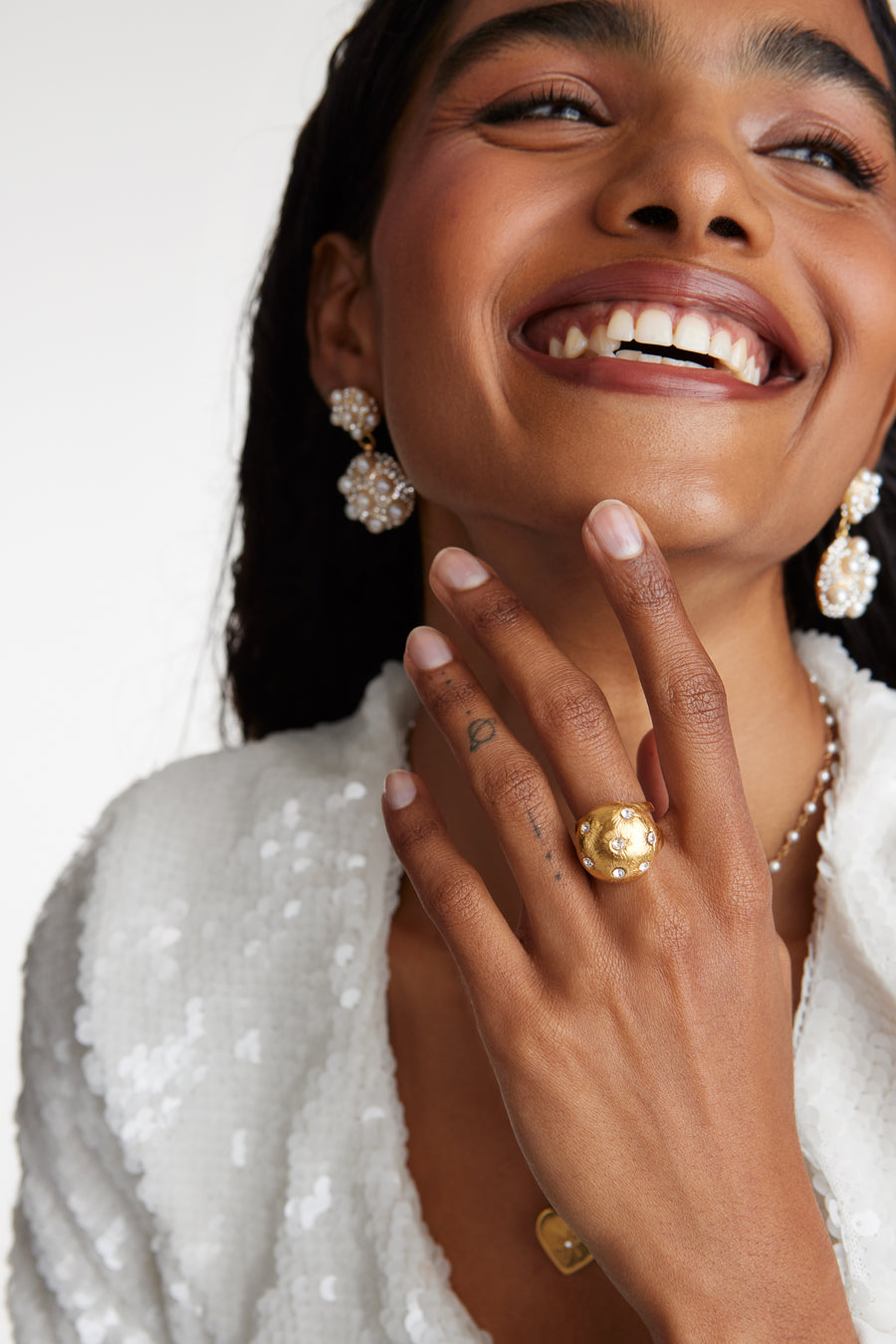 close up model shot of round gold star etched ring with clear crystal embellishment and pearl cluster earrings while model laughing