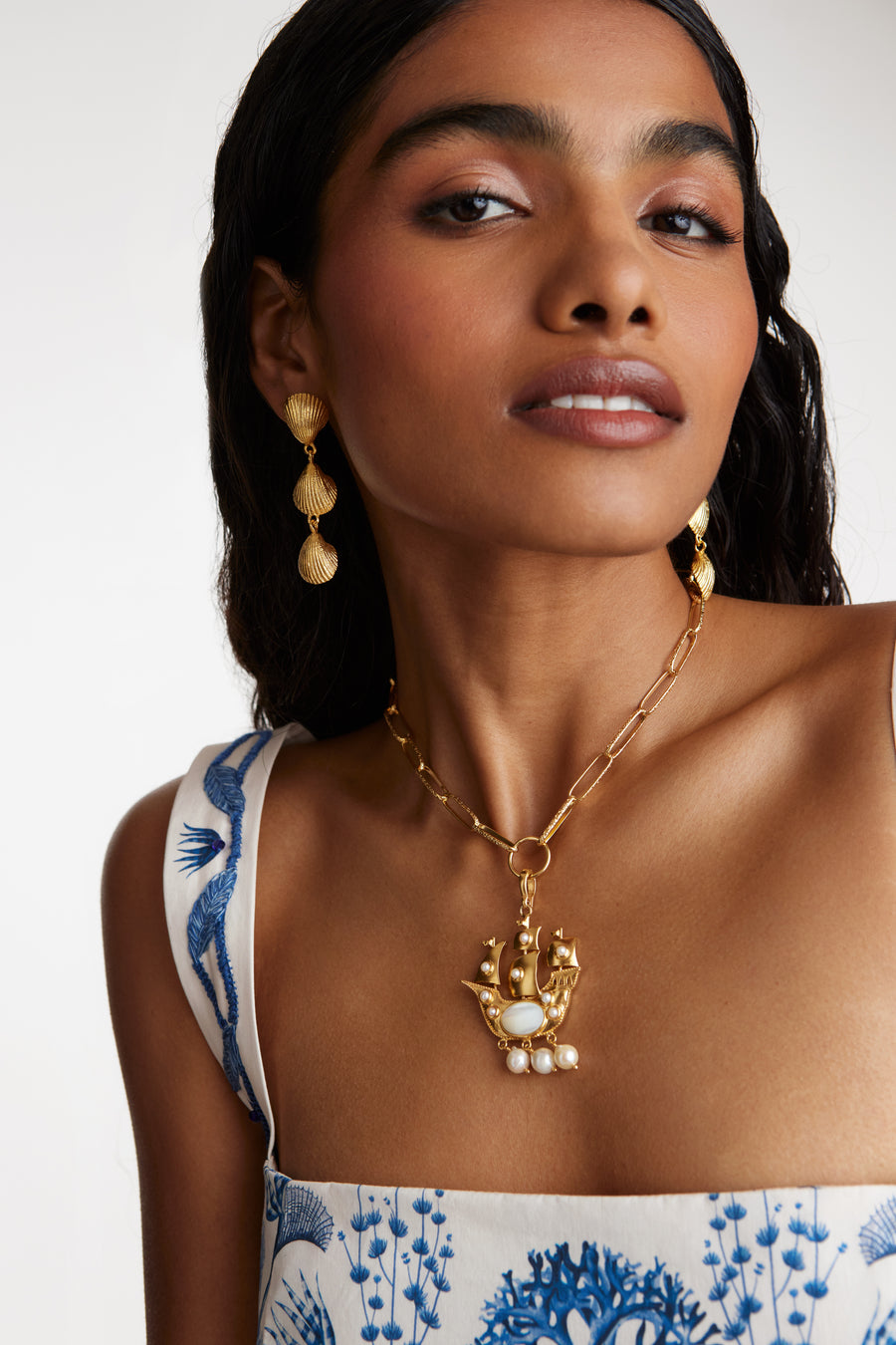 model shot wearing pearl embellished sailing ship charm on a charm necklace and wearing shell drop earrings.  
