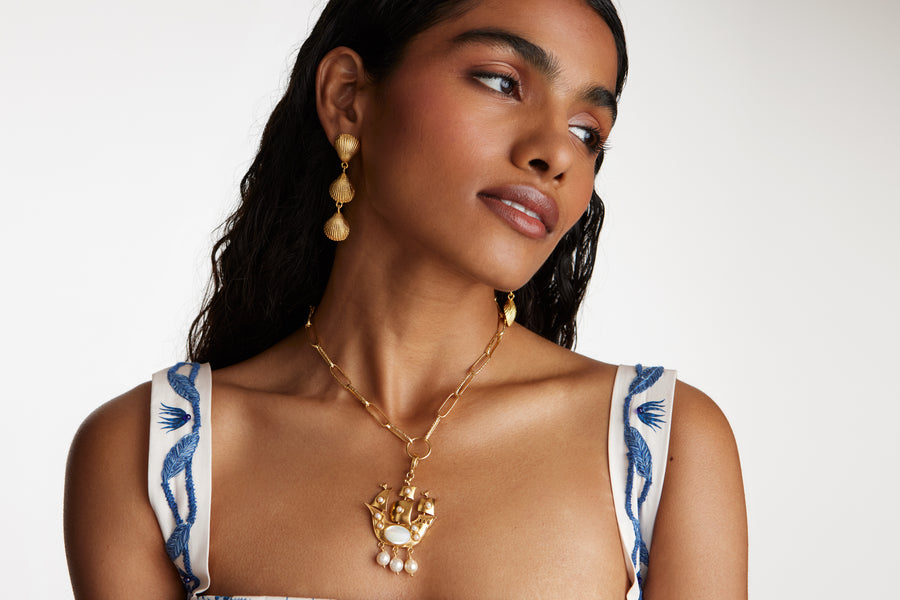 model shot looking to side wearing pearl embellished sailing ship charm on a charm necklace and wearing shell drop earrings.