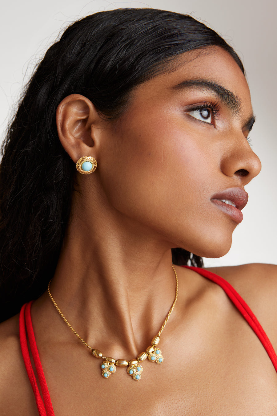 Close up side view of model shot wearing the Soru Jewellery gold rope chain necklace with gold textured beads and three turquoise embellished beaded charms. Model also wearing matching round turquoise stud earrings