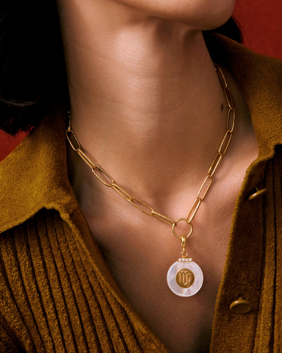 model shot of neck wearing a large mother of pearl charm with a zodiac sign on it hung on a chunky gold chain