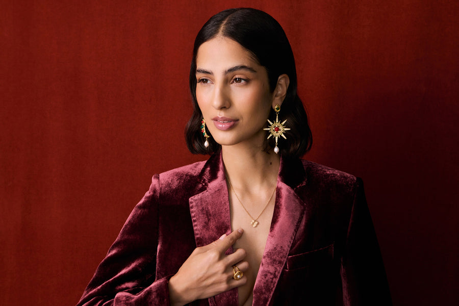 model wearing moon and star earrings and the clover necklace with a red velvet blazer and red backdrop