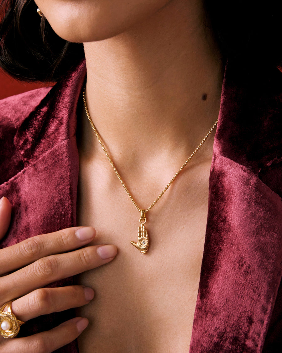 Model shot of lady wearing a charm necklace with a gold hand charm, as well as a red velvet blazer.