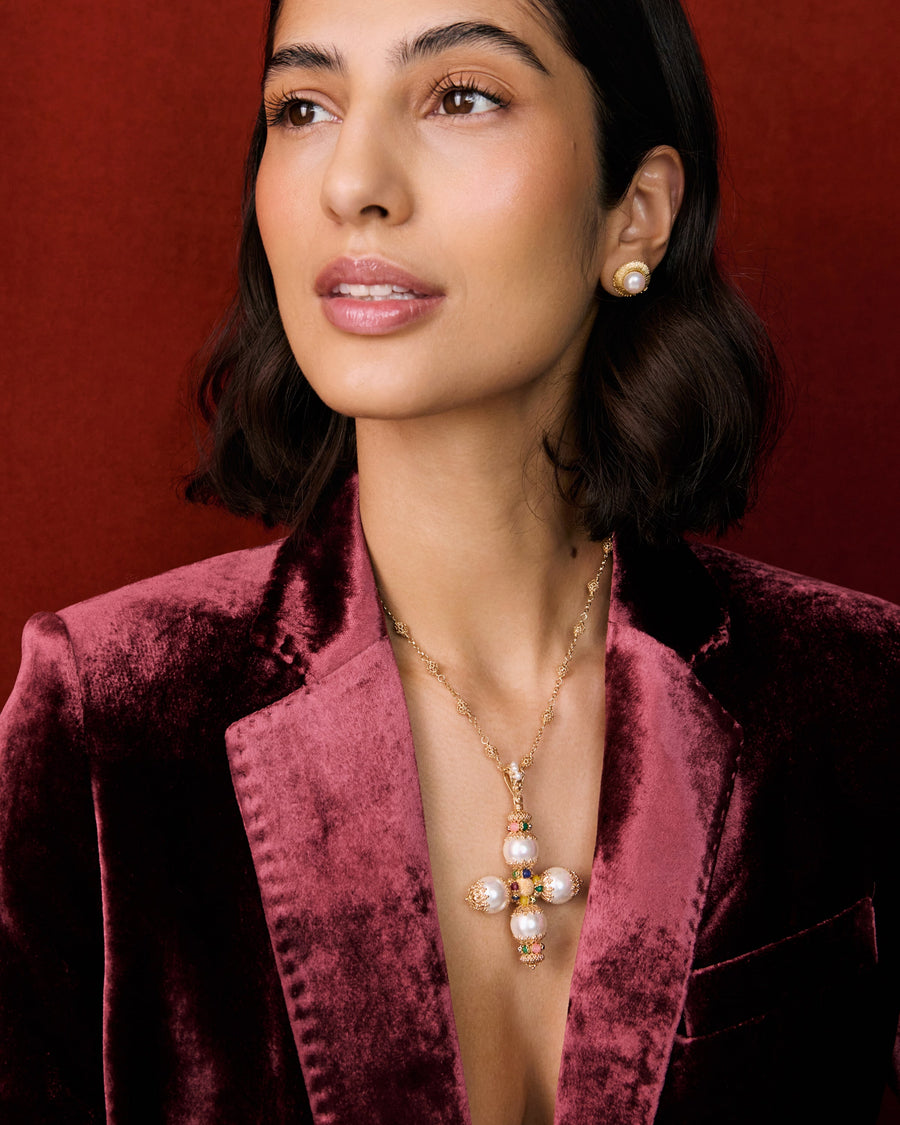 Model shot of lady wearing a gold cross pendant necklace and velvet blazer and gold ring. The necklace features pastel coloured agate gemstones, pearls and intricate filigree hung from a textured beaded chain.