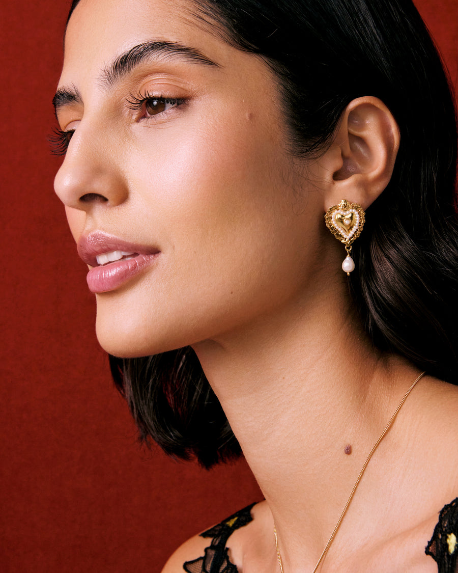 Model shot of lady wearing mini gold traditional burning heart earrings with pearl detailing, wearing a black lace top.