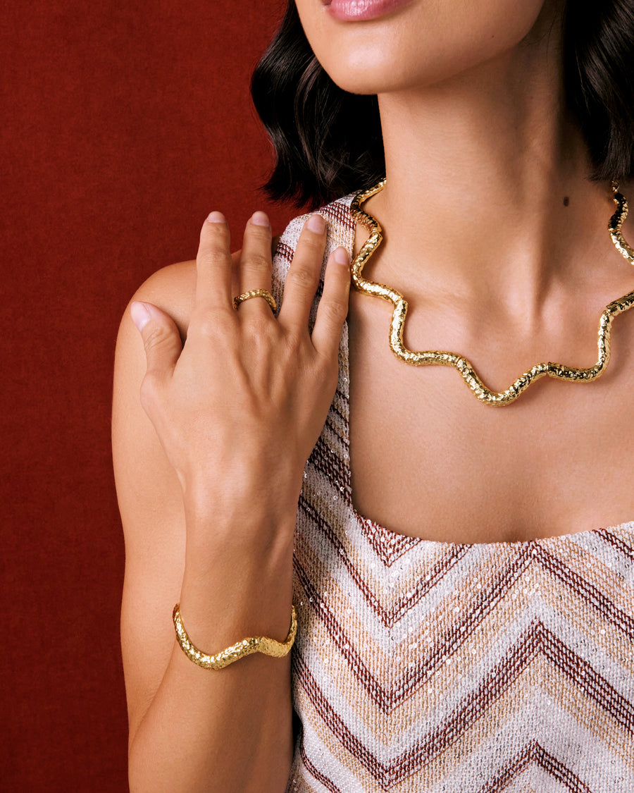 Model shot of lady wearing textured curved gold necklace, matching bracelet and ring.