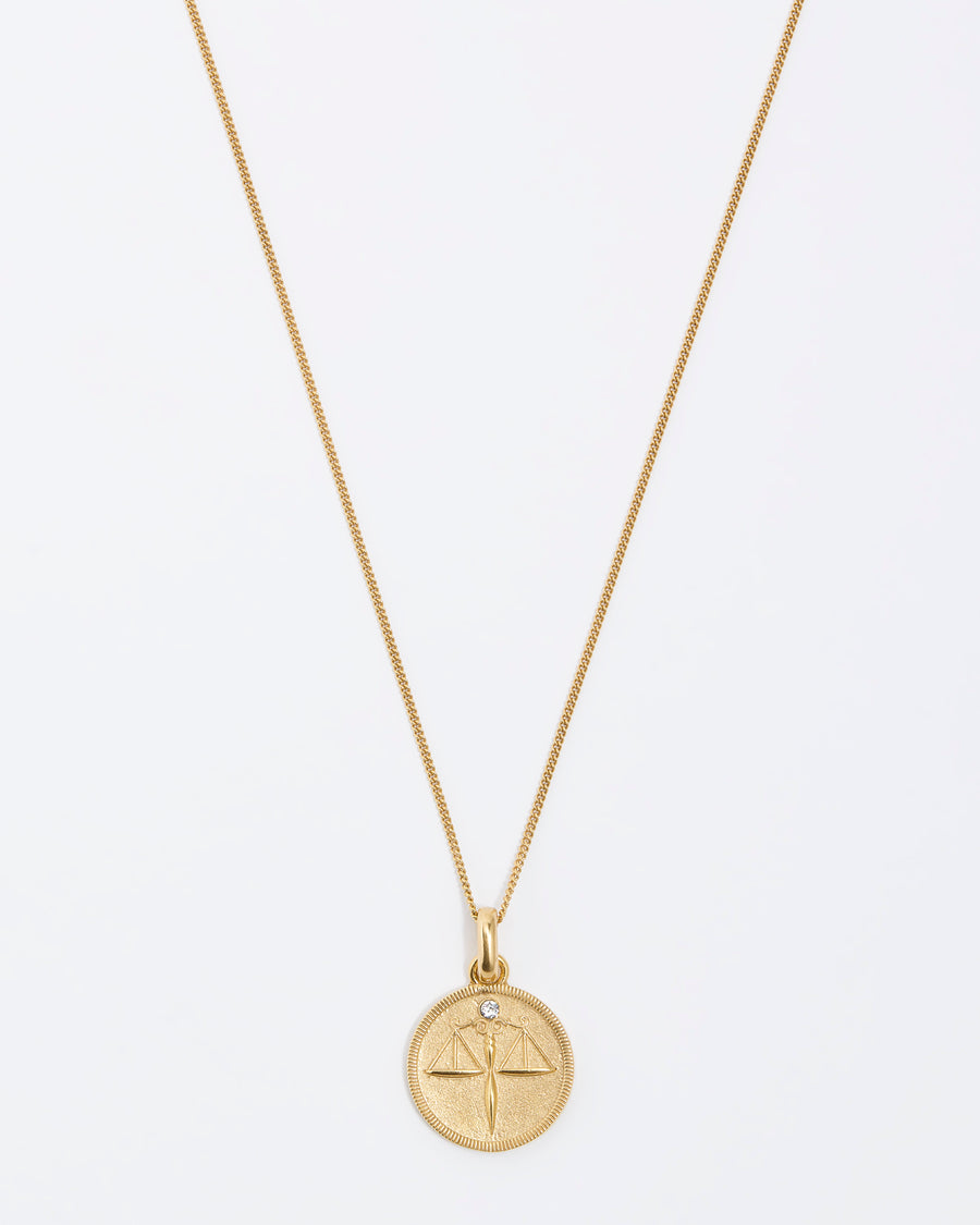 Libra scales Zodiac circular gold pendant on a fine gold chain necklace.